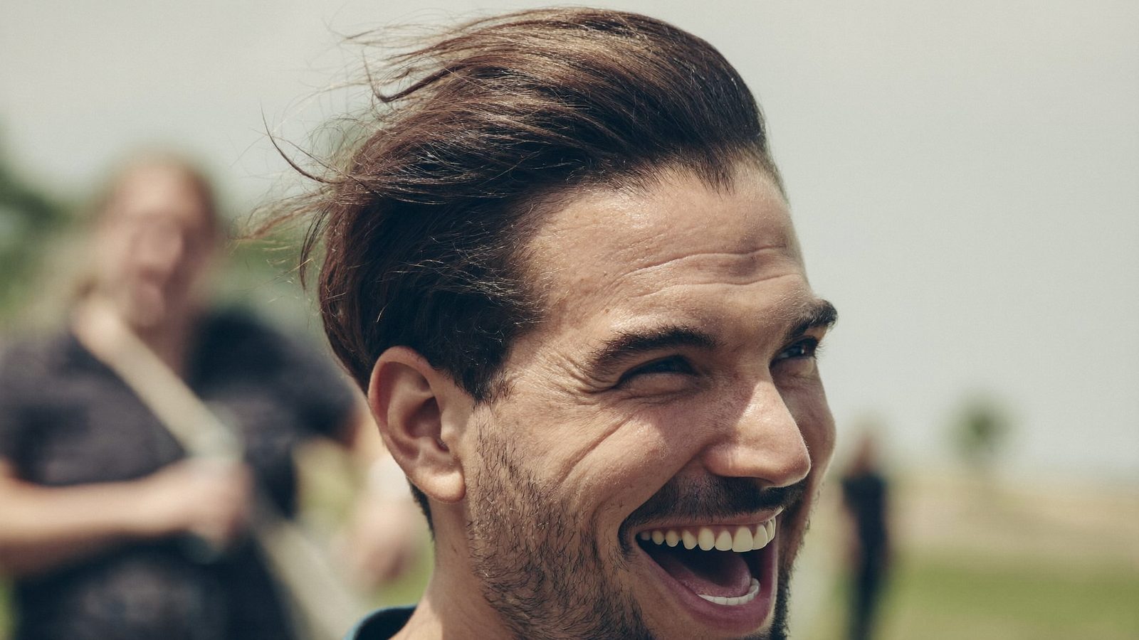 Man with a full natural hairline laughing outdoors as the wind moves his hair