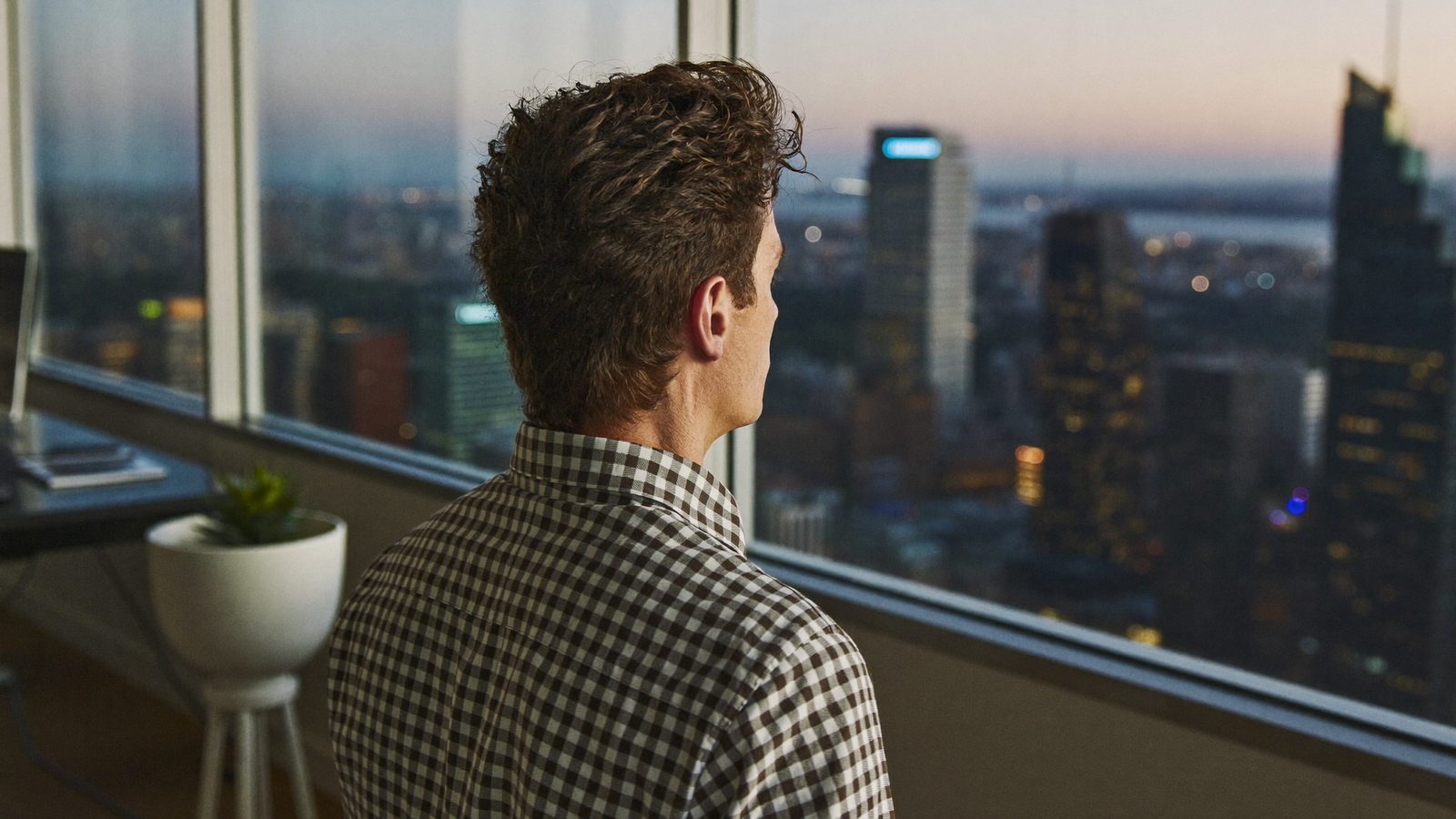 Man with thick curly hair looking out over a city skyline at dusk