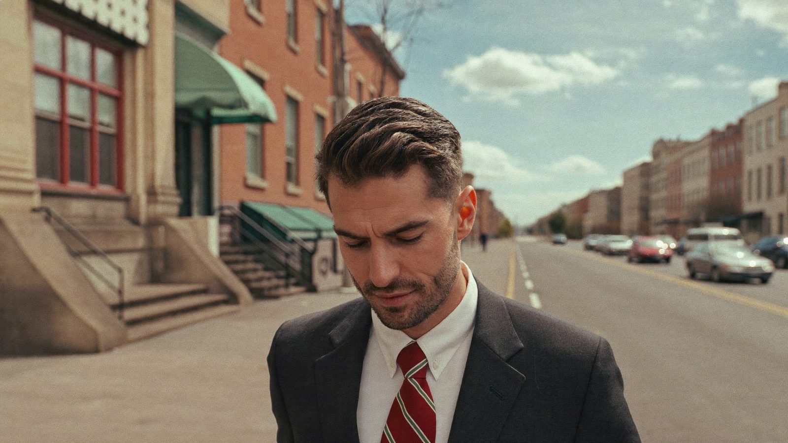 Man in a suit with well-groomed hair on a brick-lined street of row houses