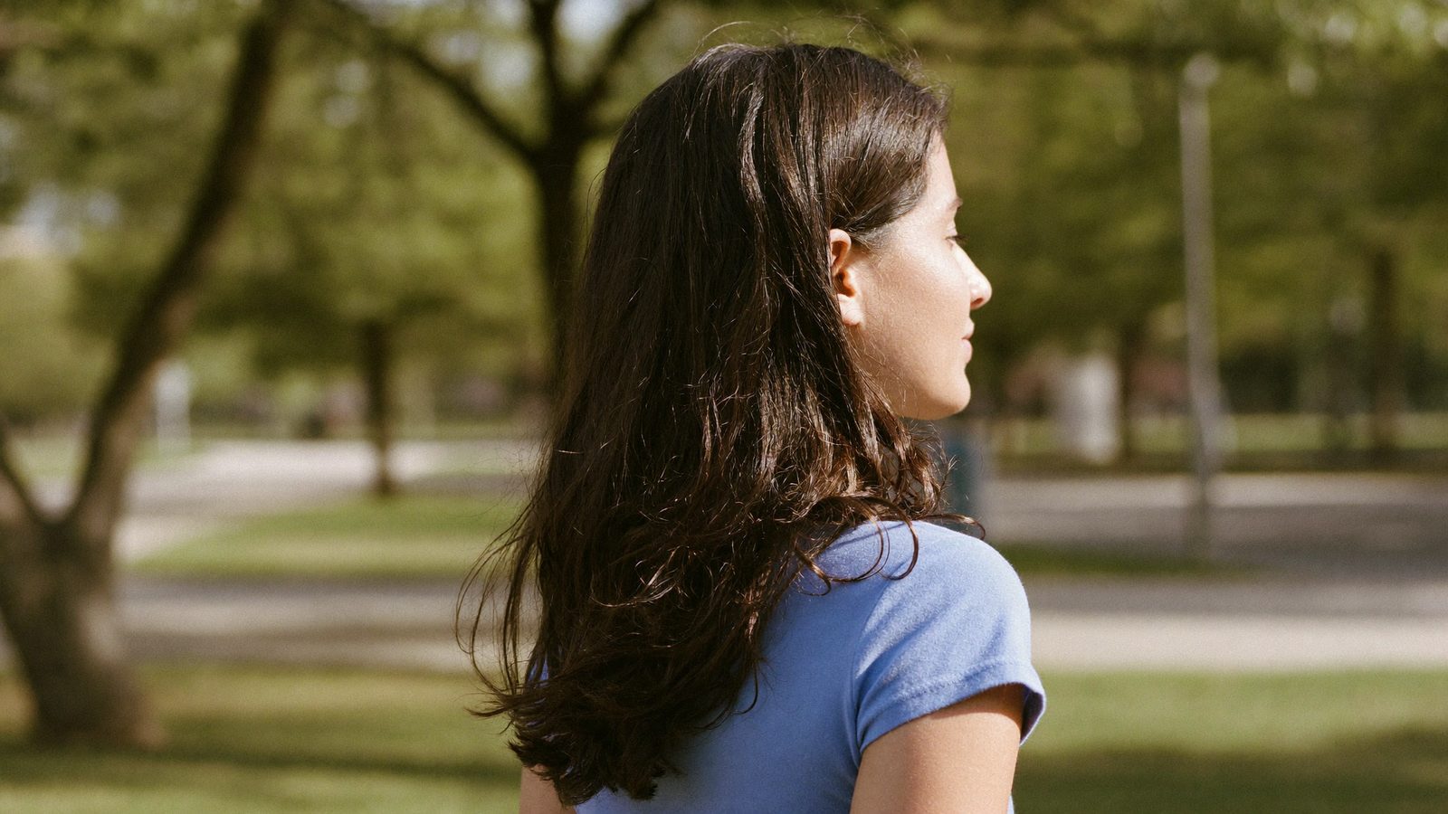 Woman with healthy shoulder-length hair walking through a sunlit park