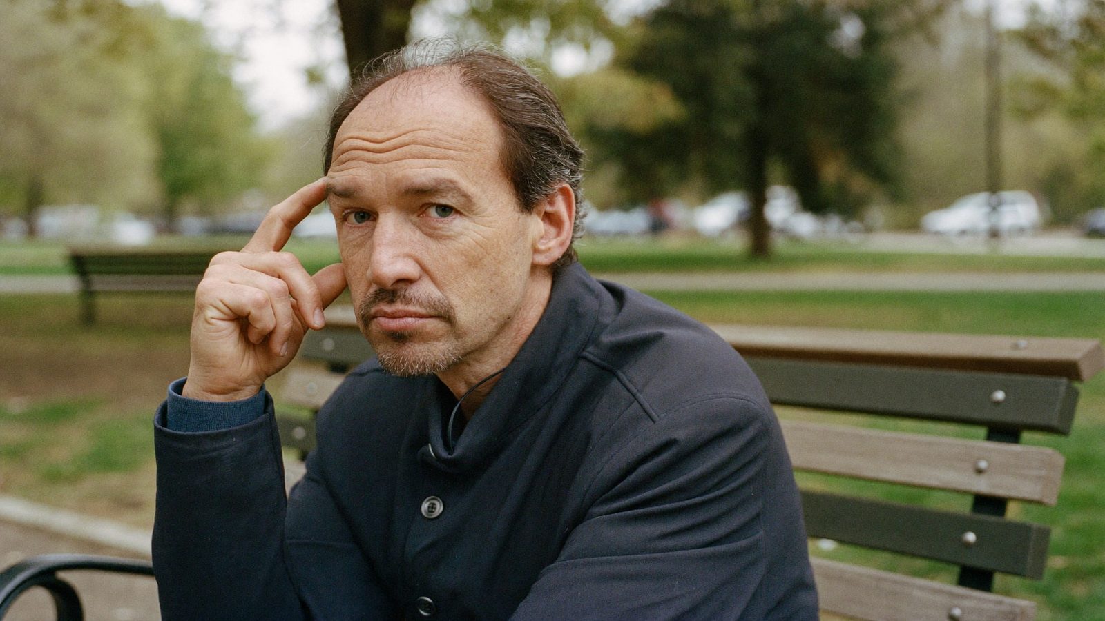 Man with a thinning hairline sitting thoughtfully on a park bench